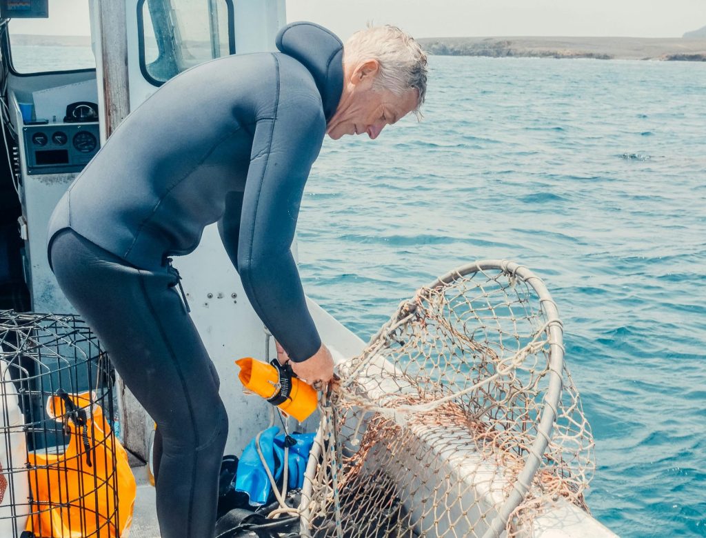 Fisherman in a wetsuit arranging nets on a boat in clear waters. Perfect for marine and fishing themes.